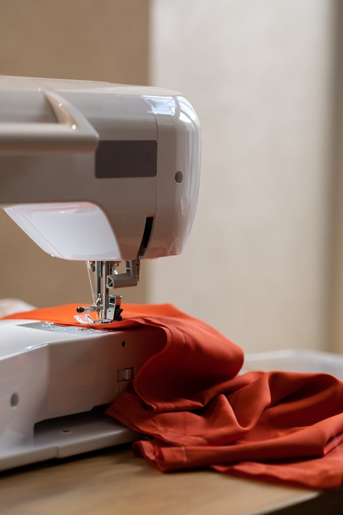 A sewing machine stitching orange fabric in a studio setting, showcasing fabric and craft.